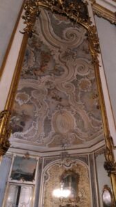 鏡に映るパステルブルーの壁の部屋、​天井の装飾がとてもロココっぽい